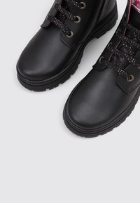 Bottes en cuir noir à lacets avec semelles épaisses et œillets en métal, montrant un gros plan de l'avant et d'une partie des lacets.