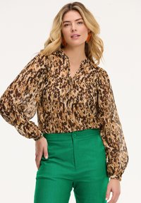 Blusa con stampa animale marrone e beige, con scollatura a V e maniche voluminose, abbinata a pantaloni verdi a vita alta. Tessuto testurizzato.