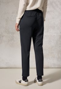 Navy pinstriped trousers with an elastic waistband, tapered fit, and back pocket detail, paired with white sneakers.
