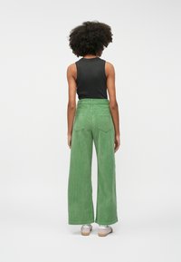Green corduroy wide-leg pants with two back pockets, paired with a black sleeveless top and silver shoes. Smooth texture and high waist design.