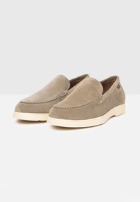 Scarpe slip-on in suede beige con punta rotonda, cuciture decorative e suola in gomma crema a contrasto. Texture liscia con dettagli minimi.