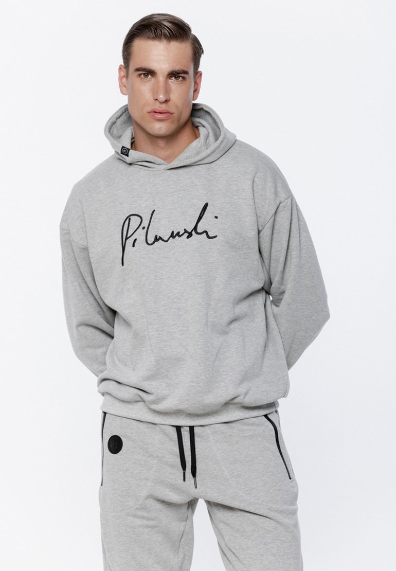 Szara bluza z kapturem z czarnym napisem, w komplecie z pasującymi szarymi spodniami dresowymi z czarnymi akcentami i zamykanymi kieszeniami.