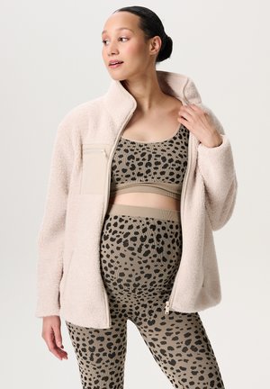 Lichtroze fleece jas met een hoge kraag en zijzak, gedragen over een beige leopardprint cropped top en bijpassende hoge taillelegging.