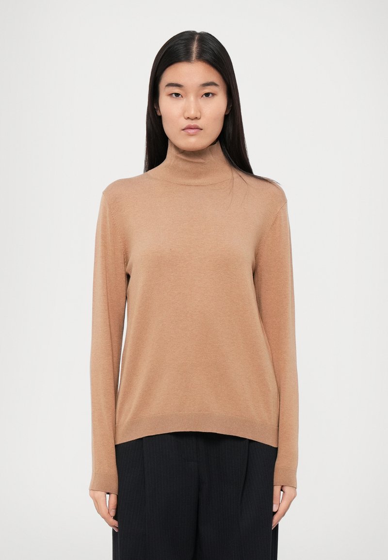 Valge pruun turtleneck-sviiter, mis on valmistatud pehmest kangast. Pikad varrukad ribaga mansetiga, vabalt lõigatud ja kergelt kaarduv hem.
