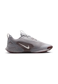 Světle šedá běžecká bota Nike s hnědými akcenty, bílým logem Nike, tečkovanou podrážkou a zavazováním na šněrování, zobrazená v bočním profilu.