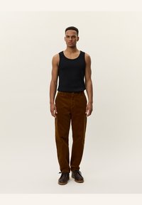 Zwarte mouwloze tanktop gecombineerd met bruine ribfluwelen broek. De broek heeft een ontspannen pasvorm en een subtiele geribde textuur. Bruine schoenen maken de outfit af.