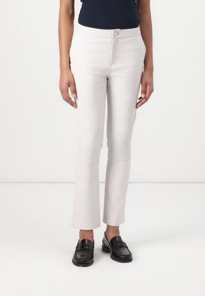 Pantalons ajustés gris clair en mélange de coton, avec une fermeture à bouton à l'avant et un ourlet légèrement évasé. Portés avec des mocassins noirs.