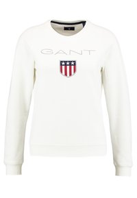 Sudadera blanca de manga larga con el texto "GANT" y un logo de escudo que presenta tres estrellas blancas sobre franjas rojas y blancas en el pecho.