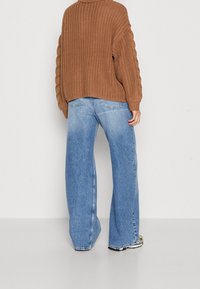 Maglione a maglia intrecciata marrone con una vestibilità over, abbinato a jeans a gamba larga blu chiaro con un finish sbiadito e design a cinque tasche.