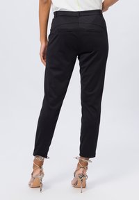 Pantalons noirs ajustés avec une coupe slim, dotés de deux poches arrière, d'une texture lisse et d'un design à la cheville, associés à des talons à sangles.