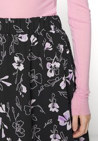 Saia preta com padrão floral roxo, tecido texturizado, cintura elástica. Top de manga longa rosa parcialmente visível.