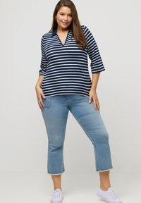 Gestreiftes Oberteil aus Baumwolle in Marineblau und Grau mit Kragen; kombiniert mit verkürzten blauen Jeans aus Denim mit ausgefransten Säumen und weißen Turnschuhen.