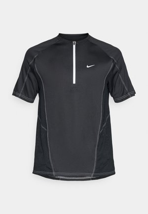 Mustat urheiluvaatteet lyhyillä hihoilla, puolivetoketju kaula-aukossa, verkkomateriaalista valmistetut sivupaneelit, valkoiset ompeleet ja pieni Nike-logo rinnassa.