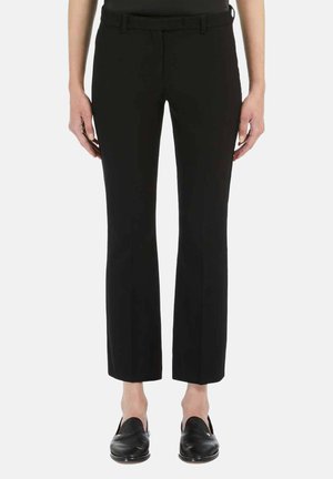 Persoon draagt zwarte, rechte, op maat gemaakte broek met riemlussen en zwarte instapschoenen, staand tegen een witte achtergrond.