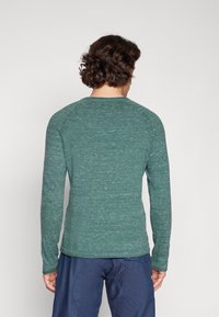 Långärmad skjorta i strukturerad grön tyg, rundad halsringning och rak fåll, tillsammans med marinblå byxor med kurvad fickdetalj.