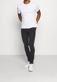 Bílé tričko s kulatým výstřihem, černé džíny s úzkým střihem a bílé tenisky. Jednoduchý design s hladkou látkou a klasickým střihem.