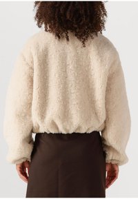 Crème kleurige pluizige jas met een textuur en een fluffy afwerking, elastische onderrand en oversized mouwen, gecombineerd met een donkerbruine rok.