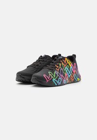 Sneakers neri con disegni di cuori in stile graffiti colorati sui lati, lacci neri e suole in gomma testurizzata, inclinati a sinistra su sfondo bianco.