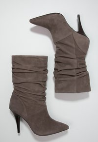 Stivaletti alla caviglia in suede grigio con design sfilato, punta affusolata e tacco a stiletto sottile. Finitura testurizzata con materiale arricciato nella parte superiore.