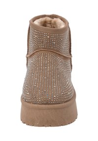 Bottine en suède marron avec un intérieur en fourrure douce et des détails cloutés. Semelle plate avec une texture antidérapante, conçue pour le confort et la chaleur.