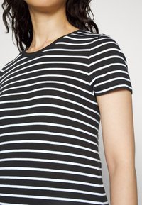 Camiseta de rayas en blanco y negro con mangas cortas y cuello redondo. El tejido parece suave y liso, con rayas horizontales uniformes.