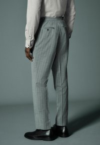 Gray pinstriped trousers made of textured fabric, featuring a tailored fit, back pockets, and black leather shoes.
