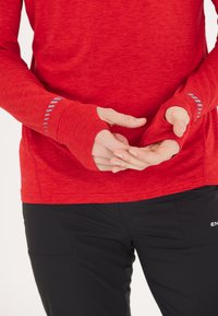 Paita pitkähiha with thumbholes, valmistettu teksturoidusta kankaasta. Sisältää vaaleanharmaita korostusviivoja hihoissa. Yhdistetty mustiin housuihin.