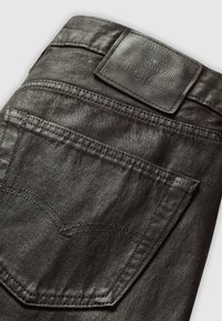 Jeans de mezclilla negra con un acabado texturizado, que presentan un parche de cuero en la cinturilla y un bolsillo trasero con un diseño de costura clásica.