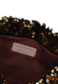 Borsa in pelle nera con paillettes dorate lungo il bordo, con un'etichetta rosa all'interno che recita "Coccinelle, Pelle Italiana Autentica."