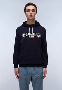 Navyblauwe hoodie met een voorzak en witte trekkoorden, voorzien van een grafische logo met een rood-witte vlag. Zachte textuur, casual pasvorm.