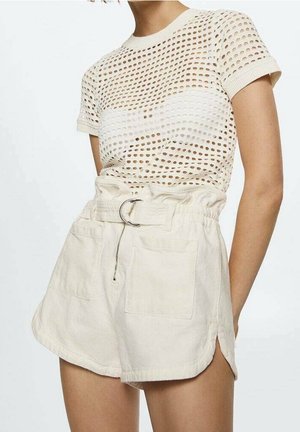 Kvinde iført beige mesh kortærmet top og højtaljede paperbag-shorts med bælte og sidelommer på lyse baggrund.