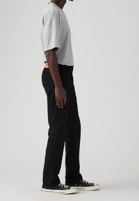 Camisa gris de manga corta, pantalones negros y zapatillas azul marino con suelas blancas. Los pantalones tienen un detalle en la cintura de color naranja. Silueta limpia y aerodinámica.