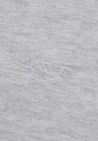 Tissu tricoté gris clair avec une texture douce et un motif subtil ; présente un logo brodé dans une teinte légèrement plus claire.