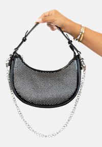 Bolso de cuero negro con un diseño perforado, acentos plateados, una correa de cadena desmontable y una forma curva para un aspecto moderno.