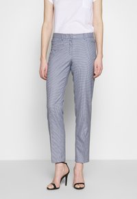 Grijze geruit broek met een getailleerde pasvorm, gemaakt van geweven stof. Heeft een gladde textuur en een platte voorkant, gecombineerd met elegante zwarte hakken.