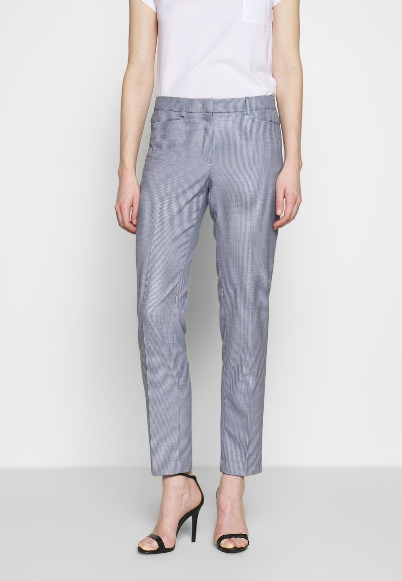 Grijze geruit broek met een getailleerde pasvorm, gemaakt van geweven stof. Heeft een gladde textuur en een platte voorkant, gecombineerd met elegante zwarte hakken.