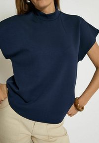Navy blue top with a high neckline, short sleeves, and a relaxed fit. Smooth texture and lightweight material.