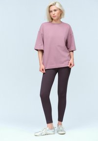 Přesně padnoucí velká mauve tričko, bavlněný materiál, kulatý výstřih, spojené s úzkými tmavě purpurovými legínami, žebrovaná textura, nošeno se stříbrnými teniskami.