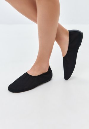 Černé ploché boty z měkké, strukturované látky, s kulatým výstřihem a nízkým podpatkem. Design je jednoduchý a ve stylu 'slip-on'.