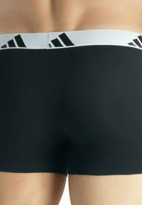 Czarne bokserki z białą elastyczną gumką w pasie, zdobione czarnym geometrycznym wzorem. Gładka faktura, dopasowany krój i długość do połowy uda.