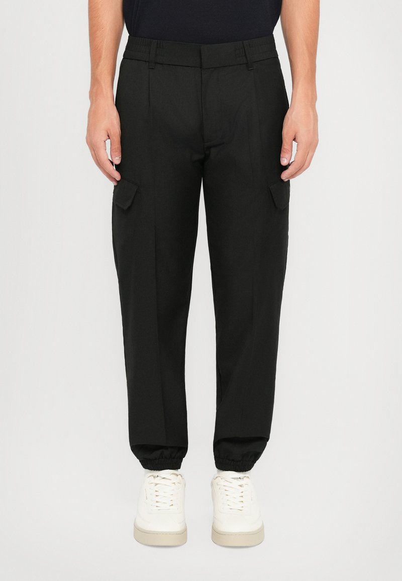 Sorte cargo bukser med elastisk talje, tapered manchetter og sidelommer. Fremstillet af et glat, let stof. Båret med hvide sneakers.
