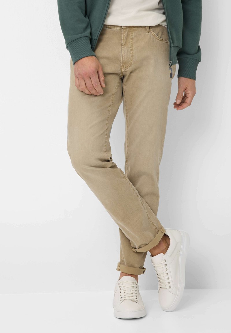 Chinos beiges en coton léger, avec une coupe droite, des coutures apparentes et des poignets retroussés, associés à des baskets blanches.
