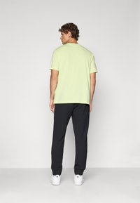 Hellgrünes T-Shirt mit kurzen Ärmeln, kombiniert mit dunklen Hosen und weißen Turnschuhen, mit Fokus auf einem lässigen und bequemen Sitz.