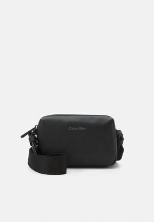 Kompakt rektangulær sort crossbody-taske med justerbar rem og sølvfarvet Calvin Klein-logo placeret centralt på forsiden.
