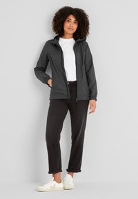 Black patterned lightweight jacket with a hood, front zipper, and pockets, worn over a white T-shirt and black rolled-cuff pants.