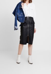 Svart läder midi kjol med framdragkedja, två fickor och en slits framtill. Kombination med en vit skjorta och en jeansjacka. Vita ankelstövlar.