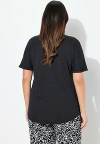 Černé tričko s krátkým rukávem a uvolněným střihem, kulatým lemem, vyrobené z měkké, lehké tkaniny. Nosené s černobílými vzorovanými kalhotami.