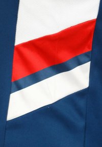 Marineblauwe stof met een diagonaal ontwerp met rode en witte strepen aan de bovenkant en een bredere blauwe streep eronder. Textuur gaas aan de bovenkant.