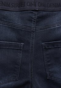 Mörkblå denimjeans med en strukturerad yta. Har en svart midja med "ONE DENIM STREET" präntat, två bakfickor och snygg sömnad.