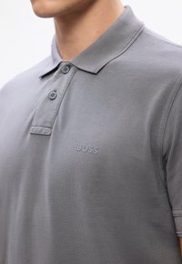 Szary polo wykonany z teksturowanej tkaniny, z kołnierzykiem, dwuknopkowym zapięciem i małym logo "BOSS" na piersi.